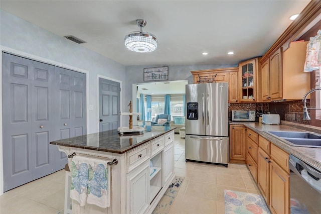 kitchen with light tile patterned floors, stainless steel appliances, a sink, tasteful backsplash, and glass insert cabinets