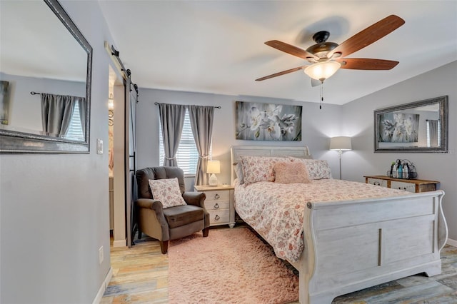 bedroom featuring baseboards, ceiling fan, light wood finished floors, and a barn door