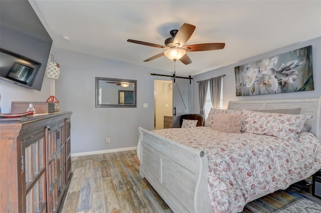 bedroom featuring a barn door, baseboards, ceiling fan, and wood finished floors