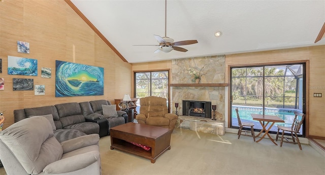 carpeted living room featuring high vaulted ceiling, a fireplace, wooden walls, and a ceiling fan