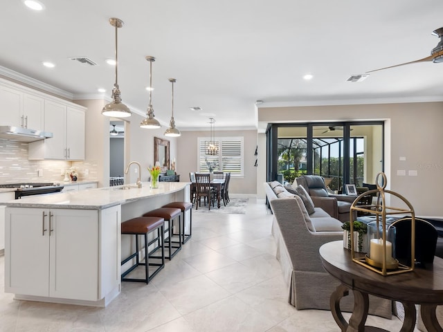 kitchen featuring tasteful backsplash, white cabinetry, hanging light fixtures, a kitchen island with sink, and crown molding