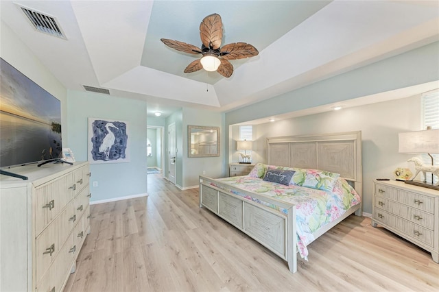 bedroom featuring ceiling fan, a tray ceiling, and light wood-type flooring