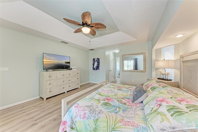 bedroom with a raised ceiling, ceiling fan, and light wood-type flooring