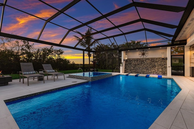 pool at dusk featuring an in ground hot tub, pool water feature, a patio, and glass enclosure