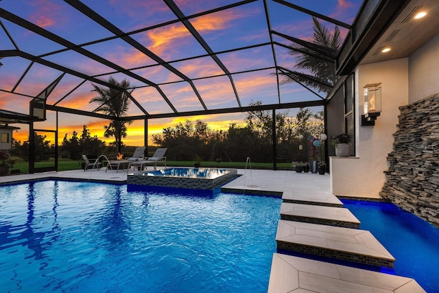 pool at dusk featuring an in ground hot tub, pool water feature, a lanai, and a patio area