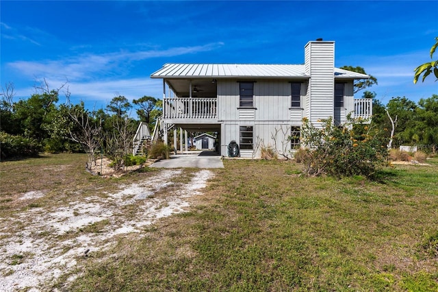 back of property with a yard, a chimney, dirt driveway, a porch, and metal roof