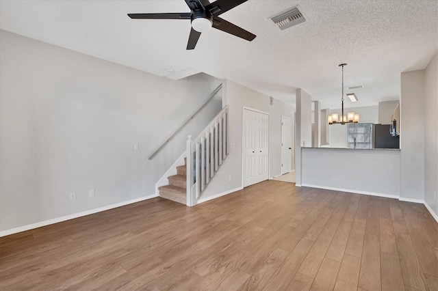 unfurnished living room with ceiling fan with notable chandelier, wood-type flooring, and a textured ceiling