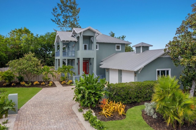 view of front facade with decorative driveway, stucco siding, metal roof, a balcony, and fence