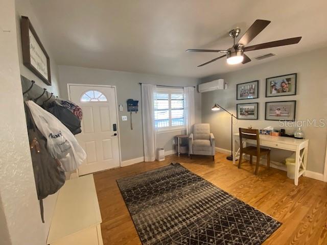 foyer entrance featuring hardwood / wood-style flooring, a wall mounted air conditioner, and ceiling fan