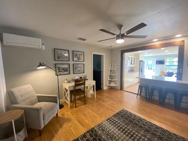 sitting room with ceiling fan, a wall mounted AC, and light wood-type flooring