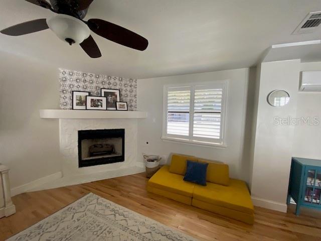 living room featuring ceiling fan, a wall mounted air conditioner, a fireplace, and hardwood / wood-style floors