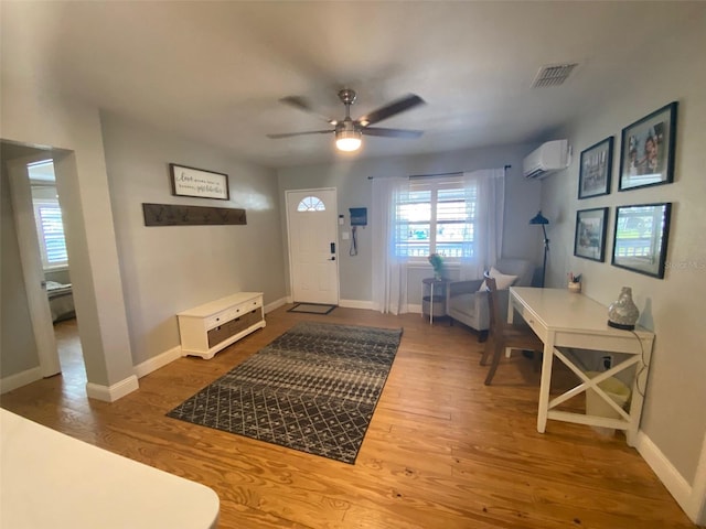 foyer entrance with a wall unit AC, wood finished floors, a ceiling fan, visible vents, and baseboards