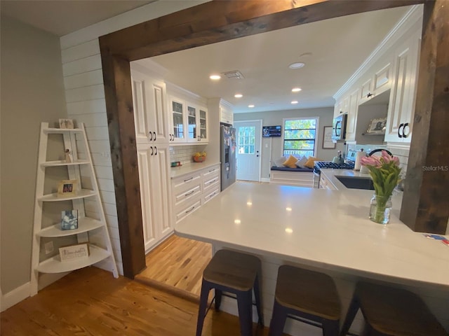 kitchen featuring stainless steel appliances, white cabinetry, light wood-style floors, and a peninsula