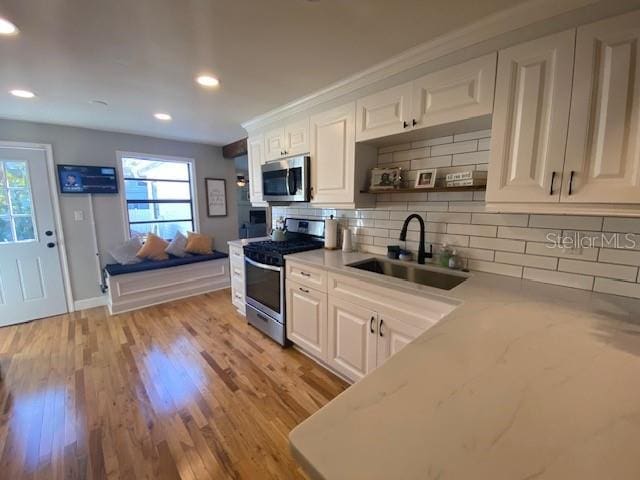 kitchen with stainless steel appliances, white cabinetry, a sink, and backsplash