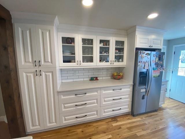 kitchen with light wood finished floors, light countertops, glass insert cabinets, white cabinets, and stainless steel fridge