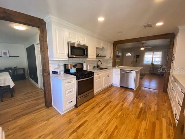 kitchen with stainless steel appliances, tasteful backsplash, light countertops, a sink, and a peninsula