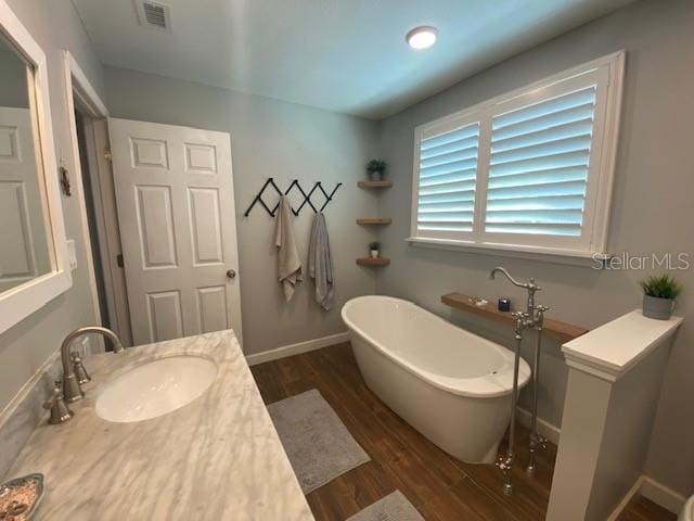 full bath featuring wood finished floors, vanity, visible vents, baseboards, and a soaking tub