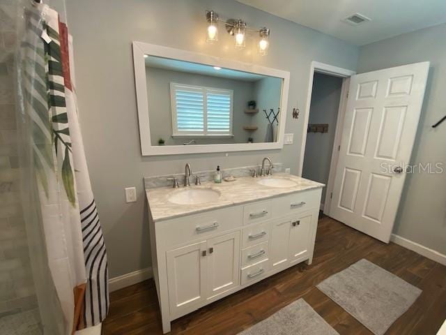 full bathroom featuring double vanity, visible vents, a sink, and wood finished floors