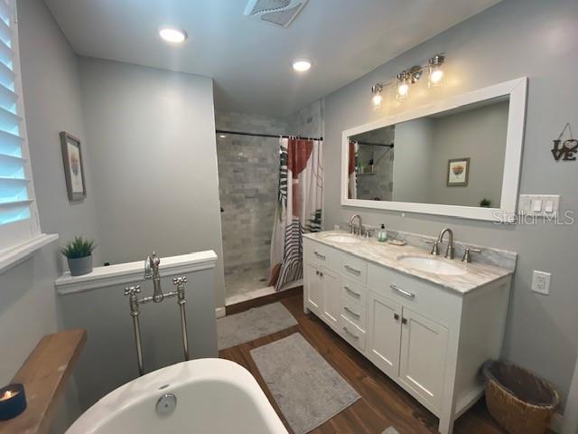 full bath with double vanity, visible vents, wood finished floors, a tile shower, and a sink