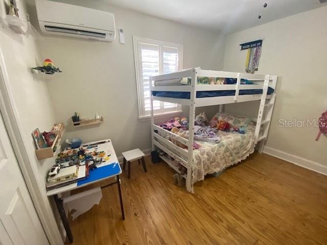 bedroom featuring a wall mounted air conditioner, wood finished floors, and baseboards