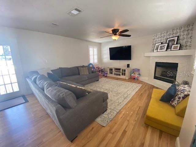 living room featuring a ceiling fan, visible vents, a fireplace, and wood finished floors