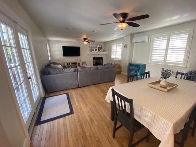 dining room with light wood-type flooring, ceiling fan, a fireplace, and a wall mounted air conditioner