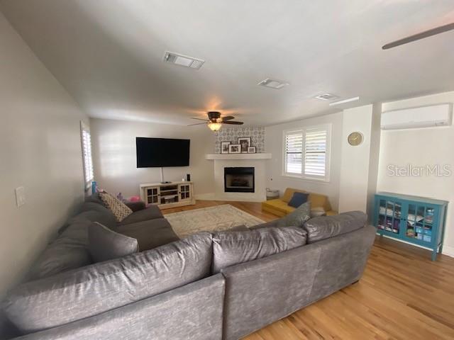 living area with a large fireplace, visible vents, ceiling fan, wood finished floors, and a wall mounted air conditioner