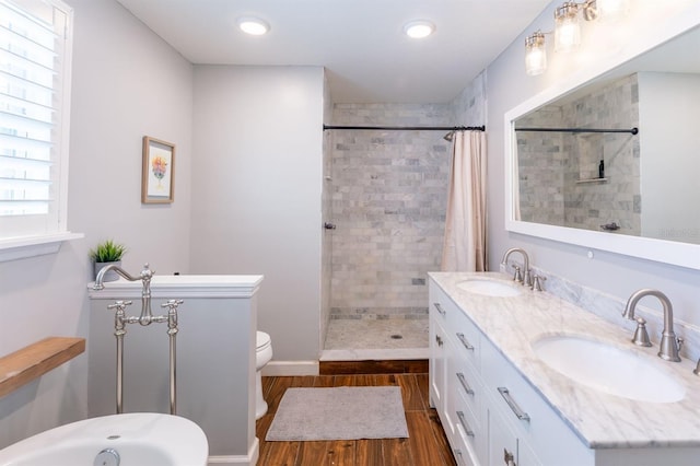 bathroom with double vanity, tiled shower, wood finished floors, and a sink