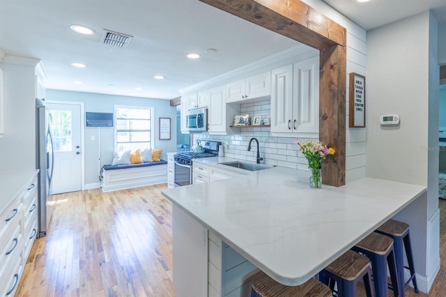 kitchen featuring light wood finished floors, a peninsula, a sink, decorative backsplash, and appliances with stainless steel finishes
