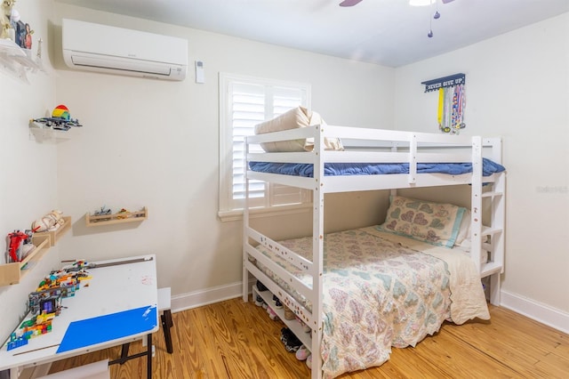 bedroom with baseboards, a ceiling fan, a wall unit AC, and wood finished floors