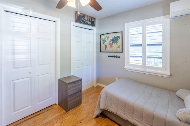 bedroom featuring a ceiling fan, light wood-style floors, two closets, and a wall mounted AC