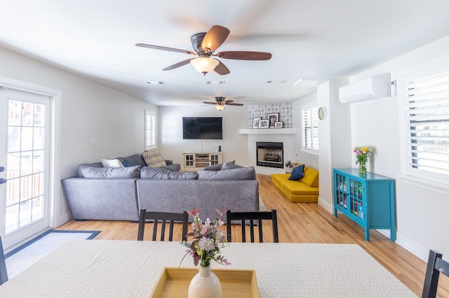living area with a wealth of natural light, visible vents, an AC wall unit, and a ceiling fan