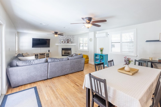 dining room with visible vents, a large fireplace, ceiling fan, light wood-type flooring, and a wall unit AC