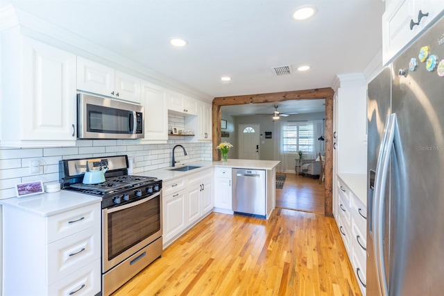 kitchen with a sink, stainless steel appliances, light wood-style floors, a peninsula, and light countertops