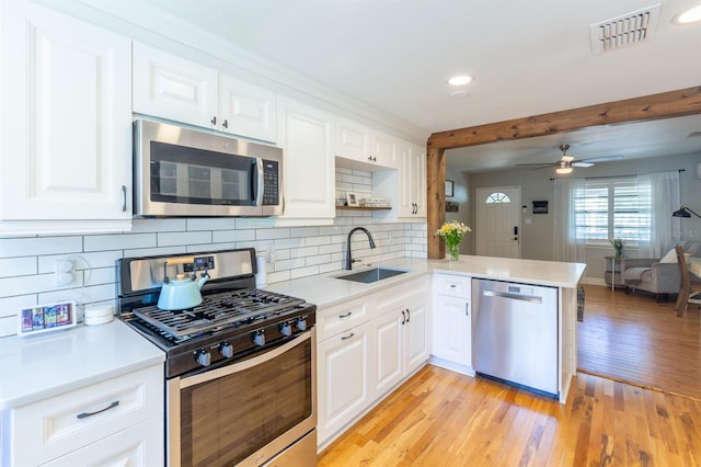 kitchen featuring visible vents, a peninsula, light wood-style floors, stainless steel appliances, and a sink