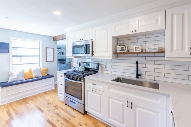 kitchen featuring tasteful backsplash, appliances with stainless steel finishes, light wood-style floors, white cabinetry, and a sink
