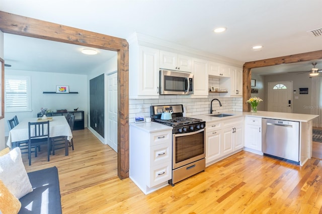 kitchen featuring backsplash, light countertops, light wood-style flooring, stainless steel appliances, and a sink
