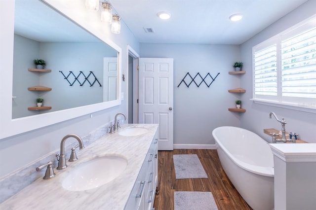 full bath with double vanity, a soaking tub, wood finished floors, and a sink