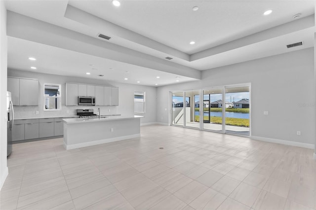 kitchen featuring gray cabinetry, stainless steel appliances, a water view, tasteful backsplash, and a center island with sink