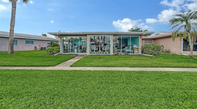 view of front facade featuring central air condition unit, a sunroom, stucco siding, and a front yard