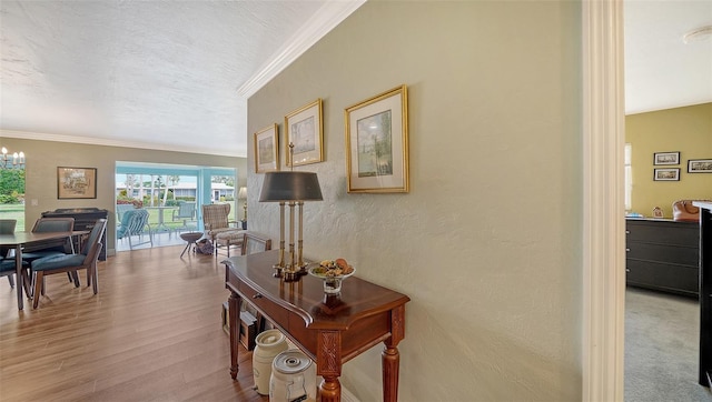 hallway with a textured wall, wood finished floors, a textured ceiling, crown molding, and a chandelier