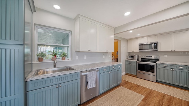 kitchen featuring stainless steel appliances, light countertops, light wood-style flooring, white cabinetry, and a sink