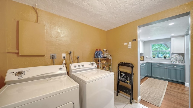 laundry room featuring laundry area, light wood finished floors, a textured wall, a textured ceiling, and washing machine and dryer