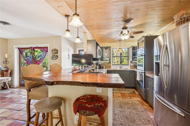 kitchen featuring gray cabinets, appliances with stainless steel finishes, butcher block countertops, a breakfast bar area, and wood ceiling