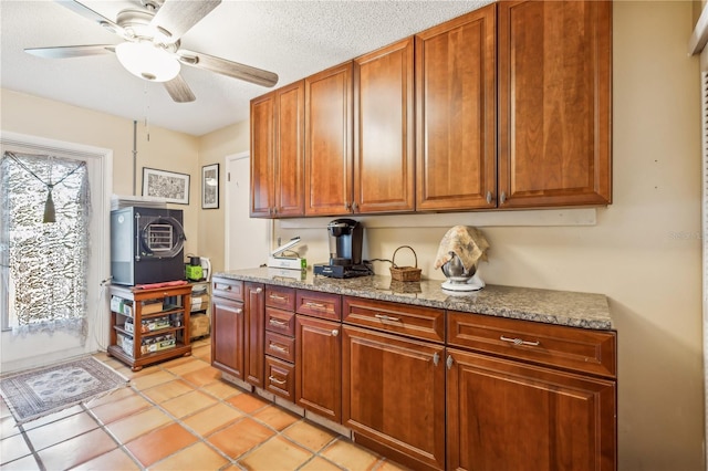 kitchen with ceiling fan, stone countertops, a textured ceiling, and light tile patterned floors