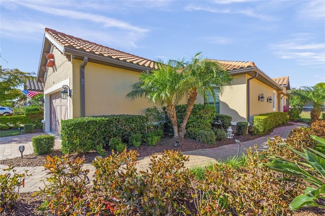 view of side of home featuring decorative driveway, a tile roof, an attached garage, and stucco siding