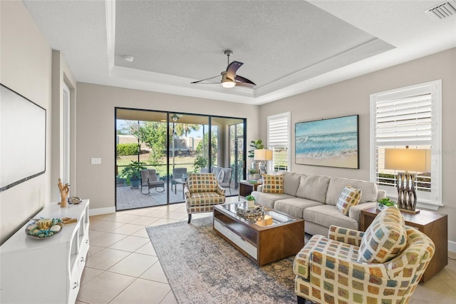 5556 Cantucci St, Nokomis, FL 34275 - living room featuring a tray ceiling, ceiling fan, light tile patterned floors, baseboards, and a textured ceiling