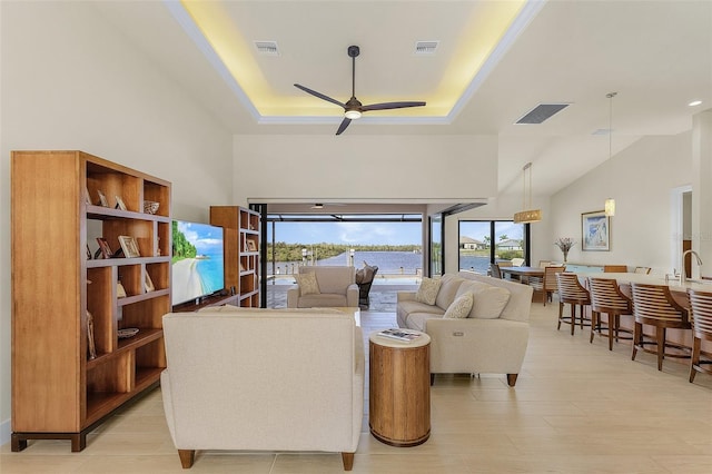 living room with a towering ceiling, a raised ceiling, and ceiling fan