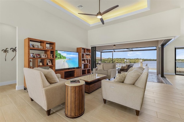 living room with ceiling fan, a tray ceiling, light hardwood / wood-style floors, and a high ceiling