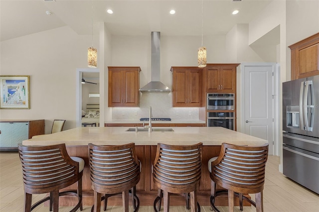 kitchen featuring pendant lighting, stainless steel appliances, an island with sink, decorative backsplash, and wall chimney exhaust hood